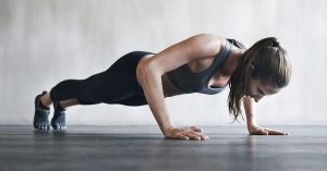 A person doing push-ups on a gym floor with a concerned expression.